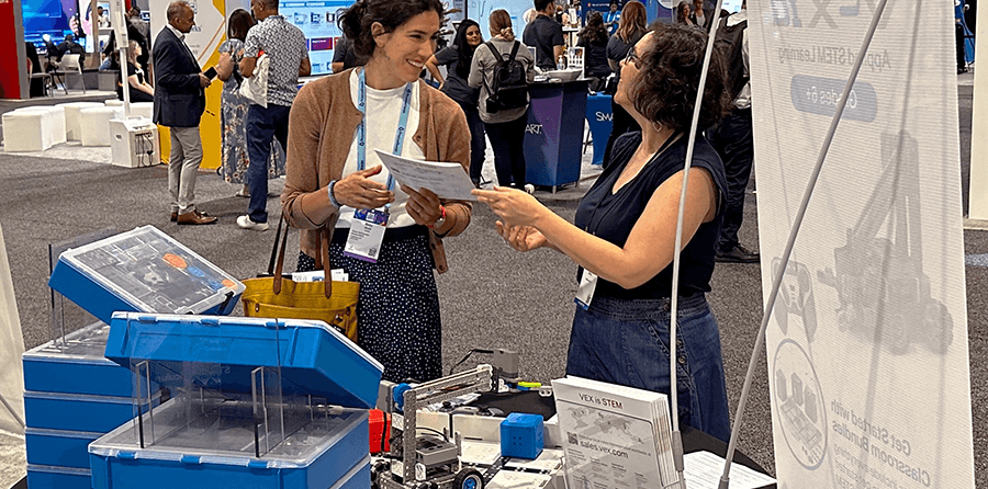 Two teachers in a conference setting talking to each other with a VEX IQ Robot kit nearby.