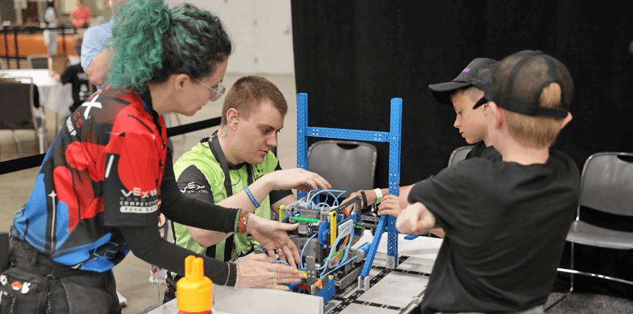 VEX IQ Competition Event Inspectors touching and looking at a robot on a table with the team of two boys watching on the right.