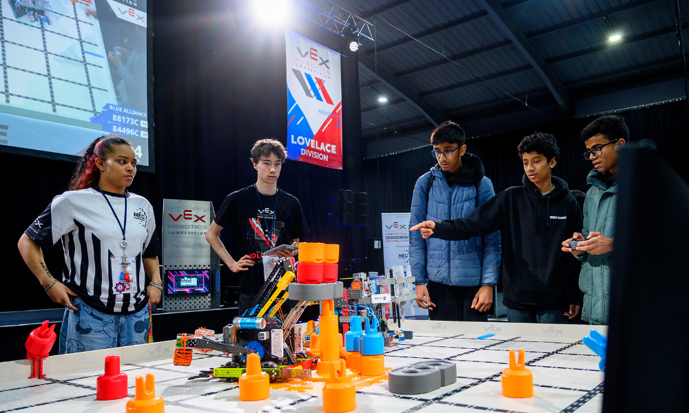 A team talks to a Head referee and volunteer at a field at the end of a match, with a team member pointing to the robot on the field.