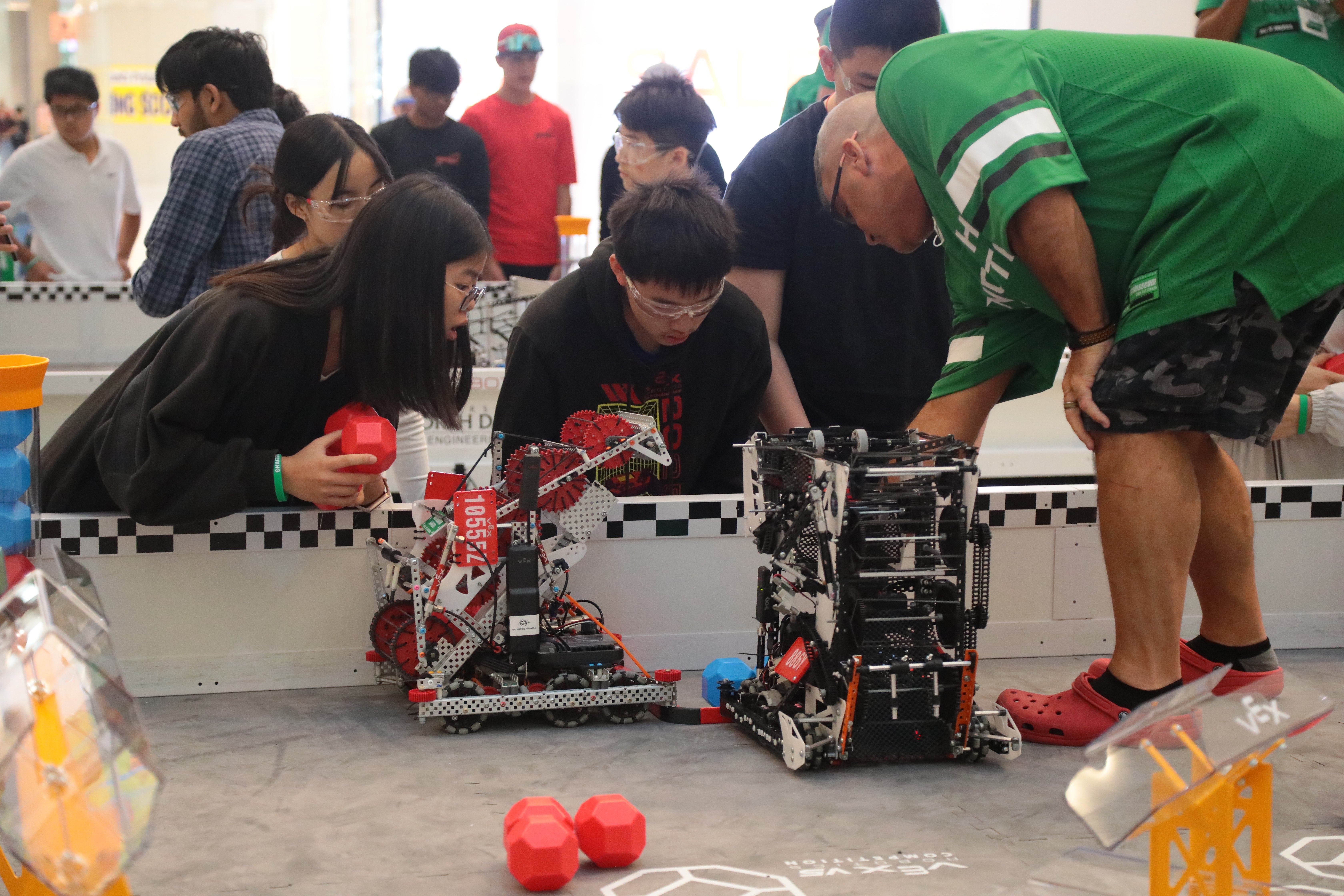 A Head Referee stands on a Field at the end of a match, pointing to the front of the robot, as the team looks on closely to determine its end position.