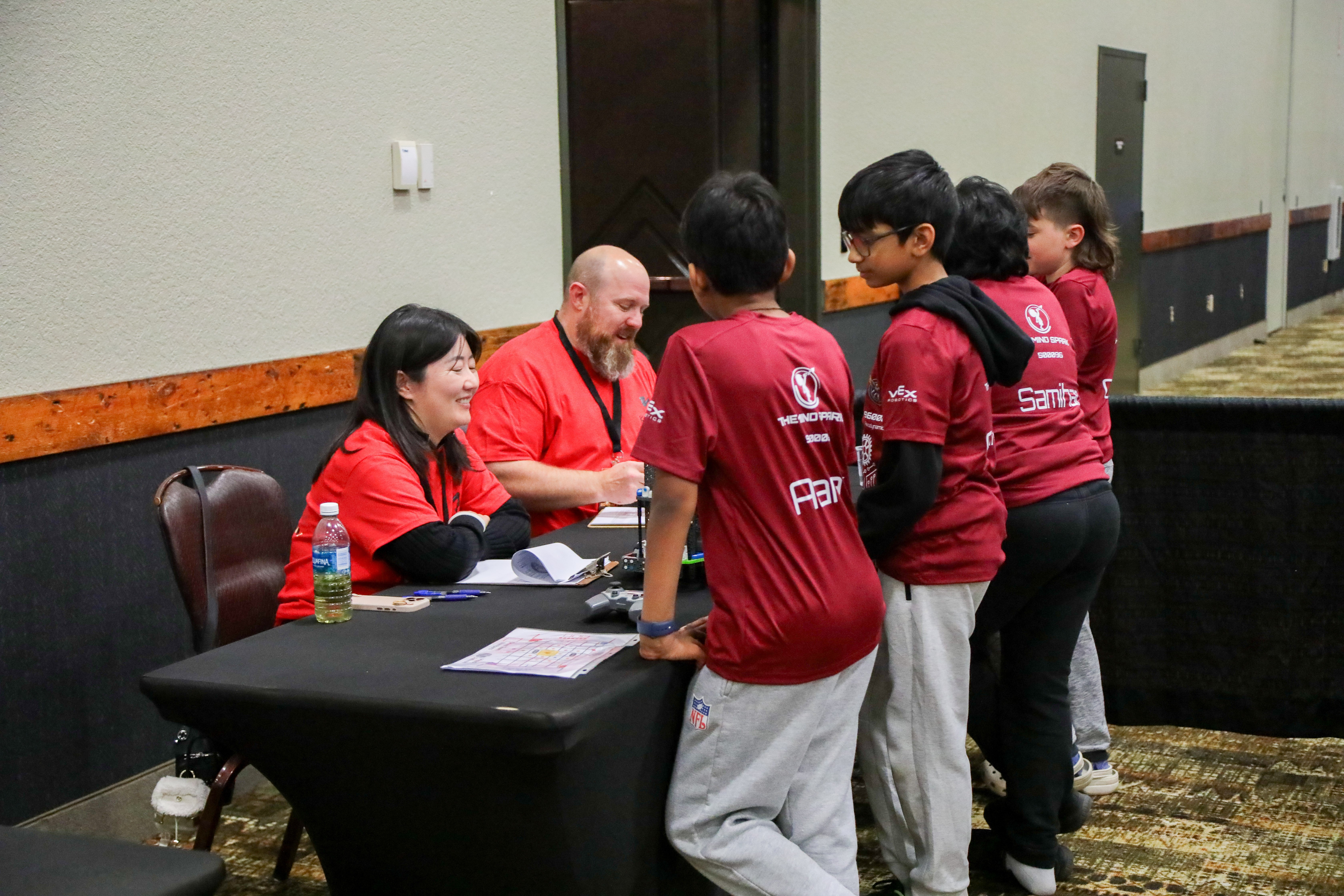 A team of four IQ students stand talking to smiling judges at a table telling them about their robot during the event.