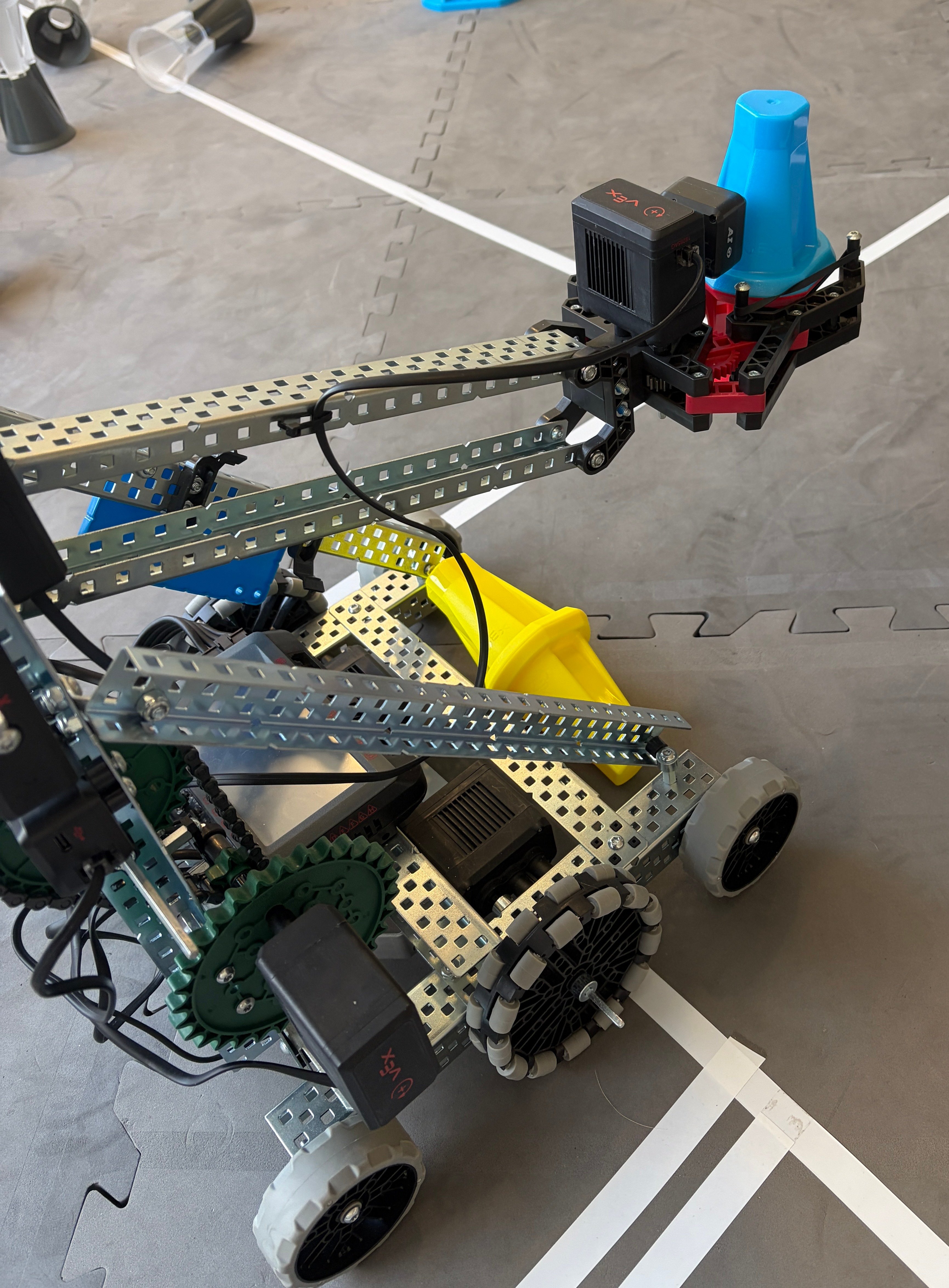 A v 5 robot in an override game. The arm of the robot is raised and holding a pin. The base of the robot has a concave area where another pin can be seen.
