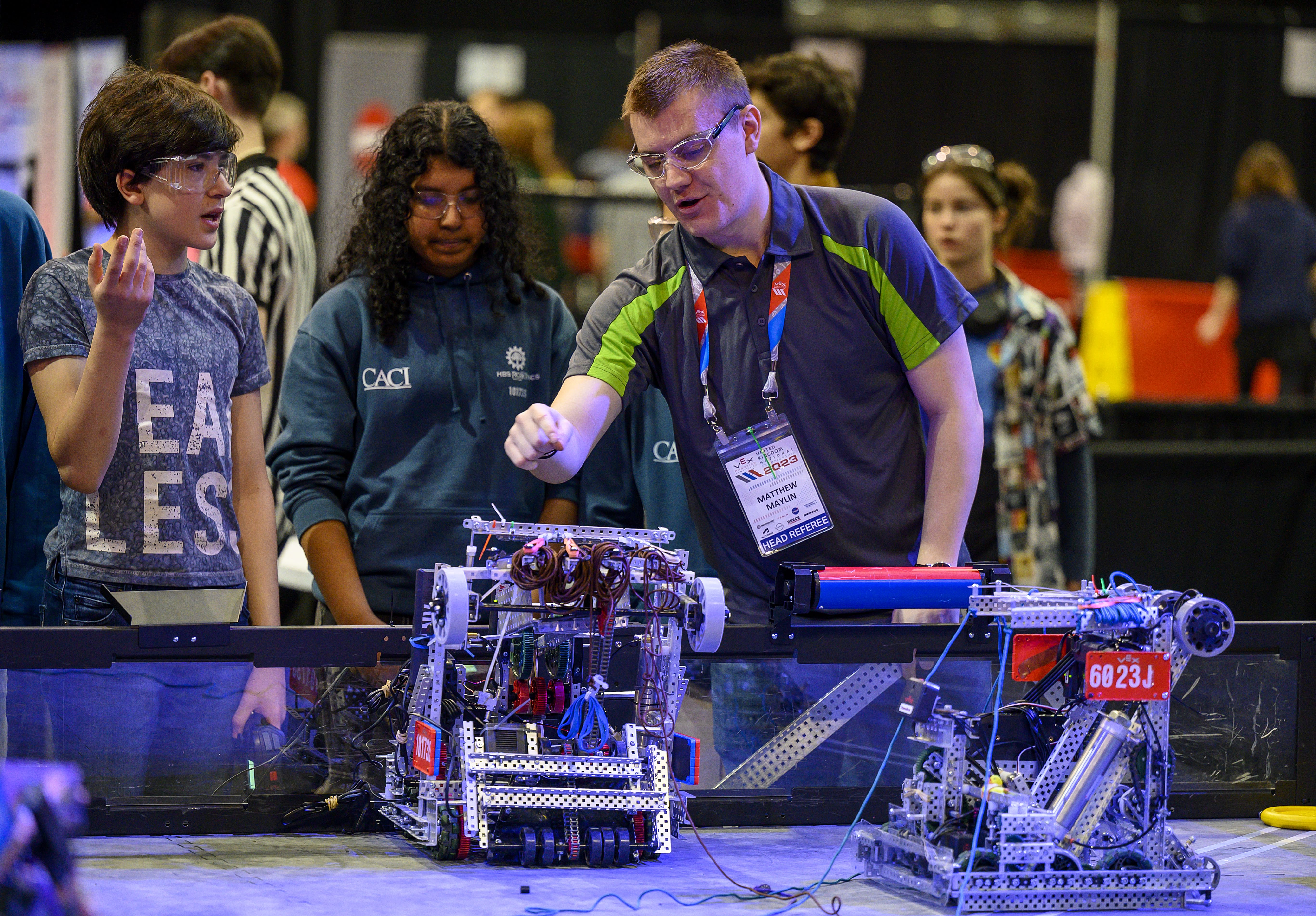 A head referee with two students at the side of a field. The Head referee is discussing the robot with the team.