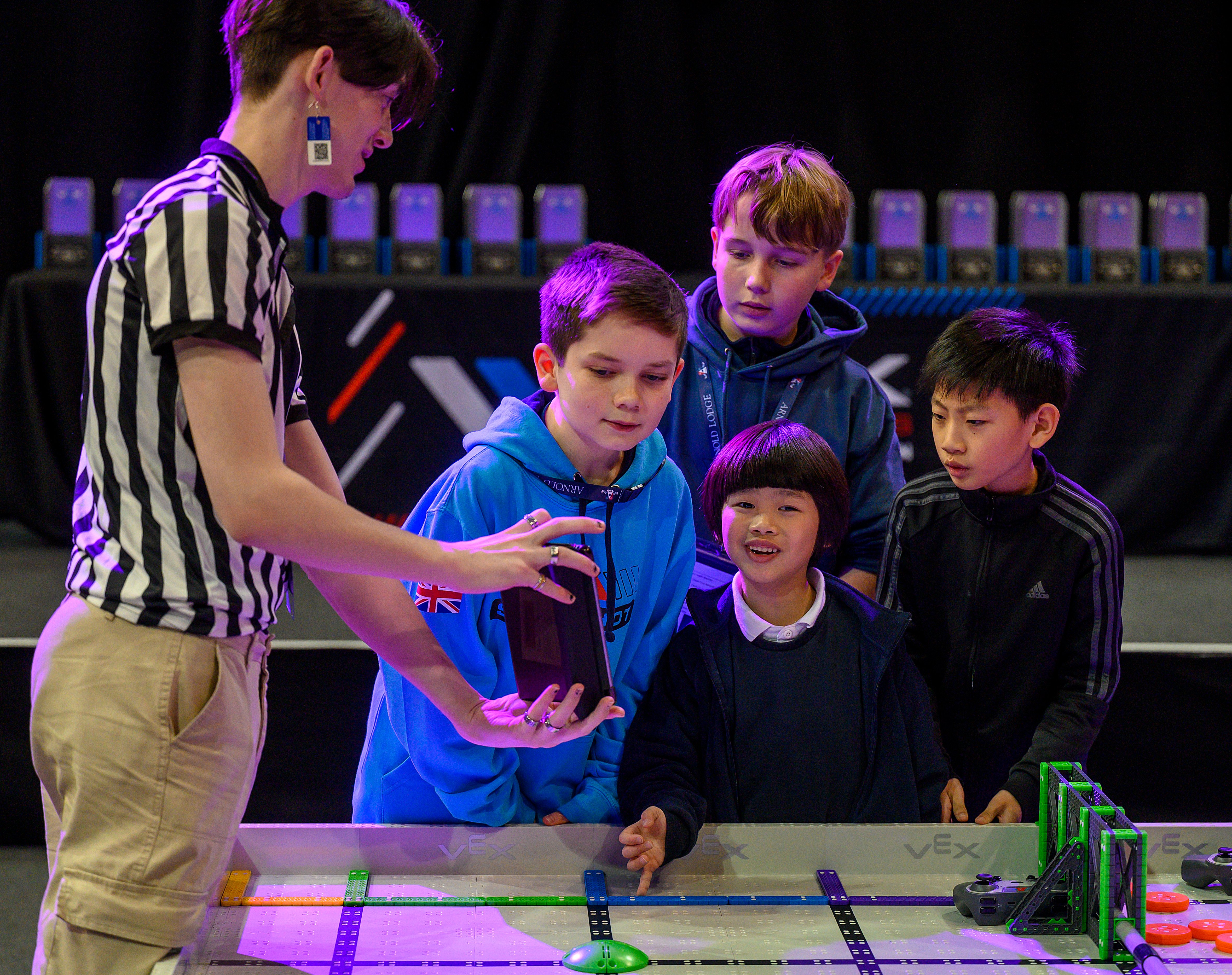 A referee next to a field shows the final score to a group of kids.