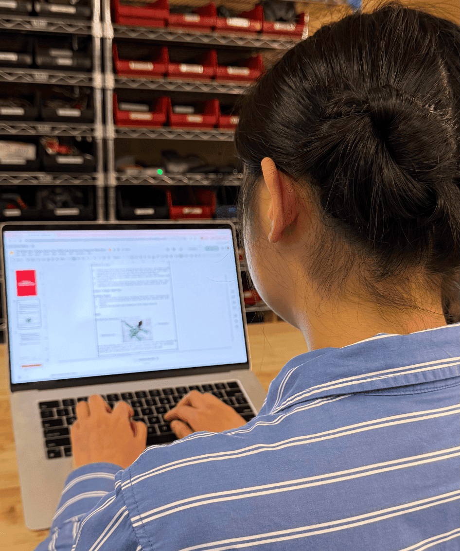 A student works on a digital engineering notebook on a laptop. The laptop is on a table in an engineering workspace.
