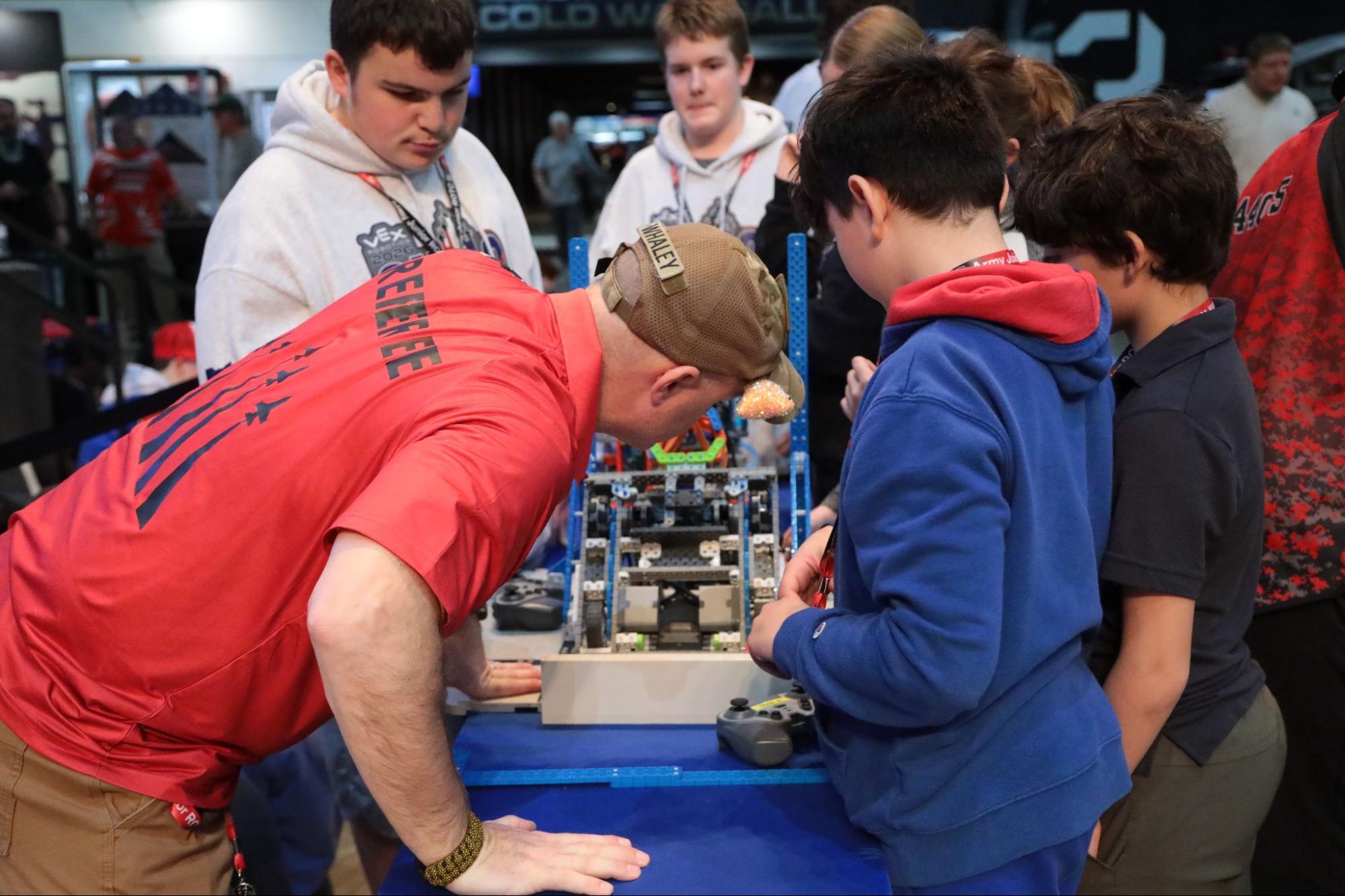 A Head Referee closely inspects a robot, while team members look on.
