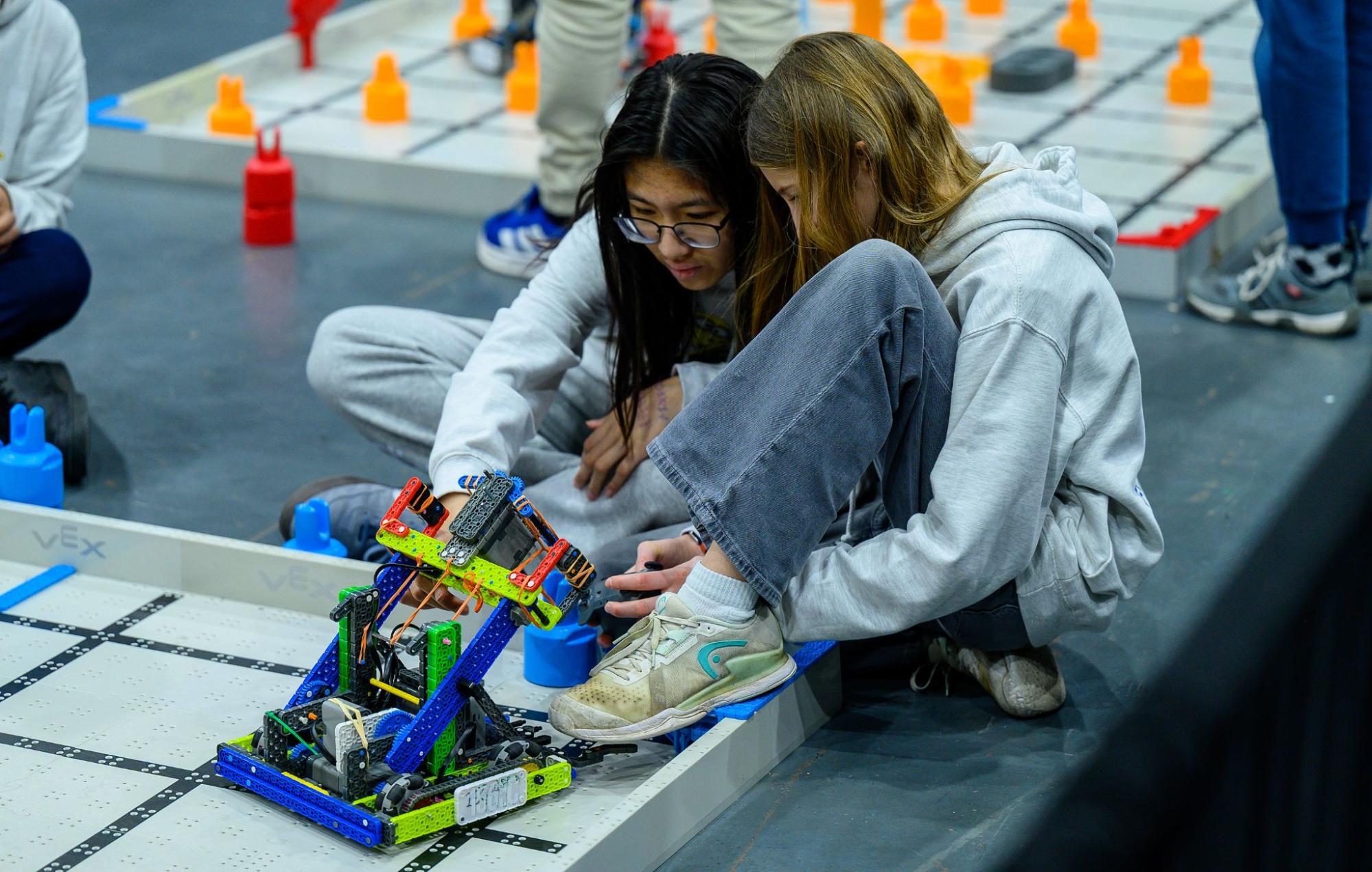 Two students sit at the edge of a Field, adjusting their robot before a match.