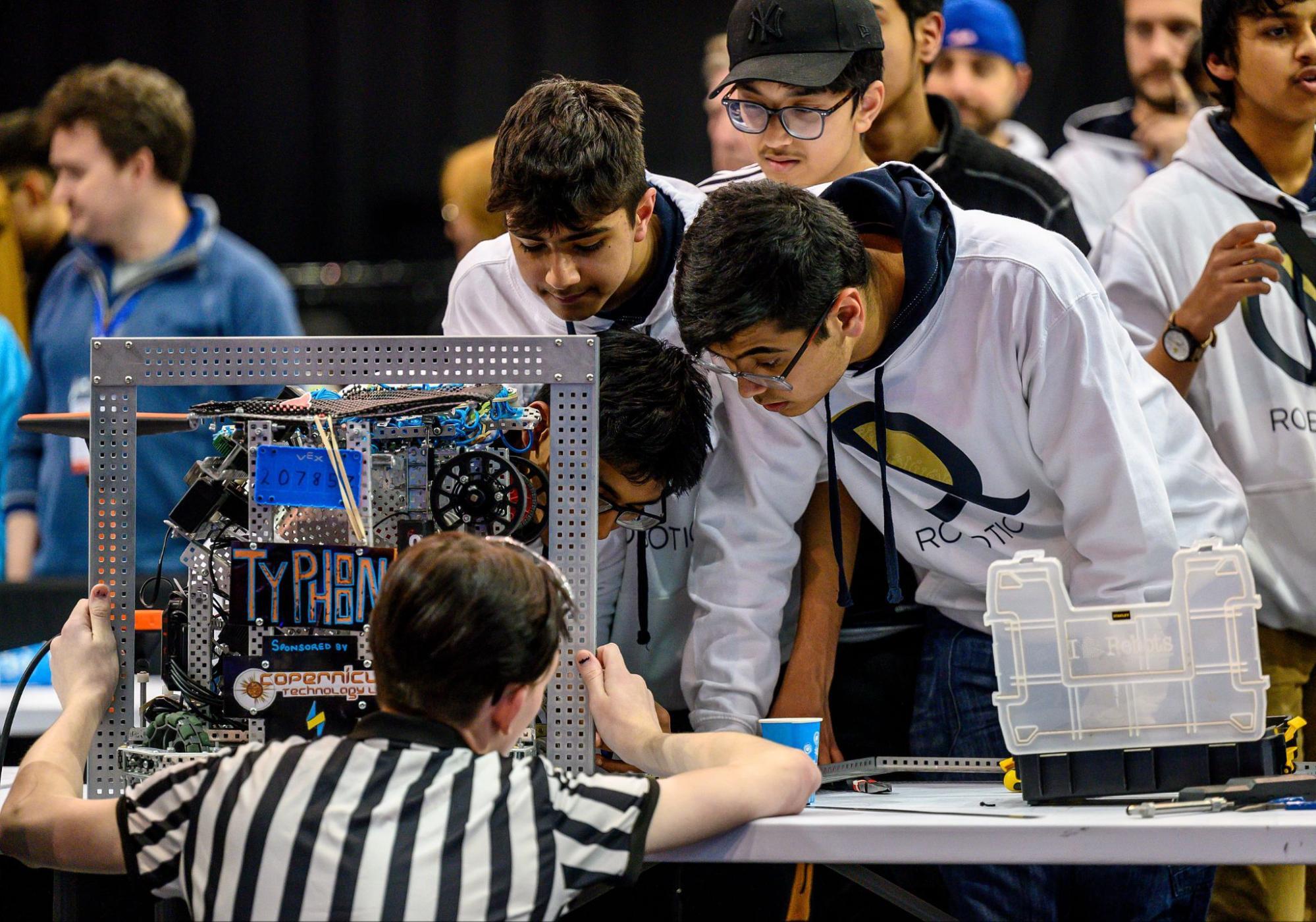 A referee holding a sizing tool up to a robot during the inspection process.