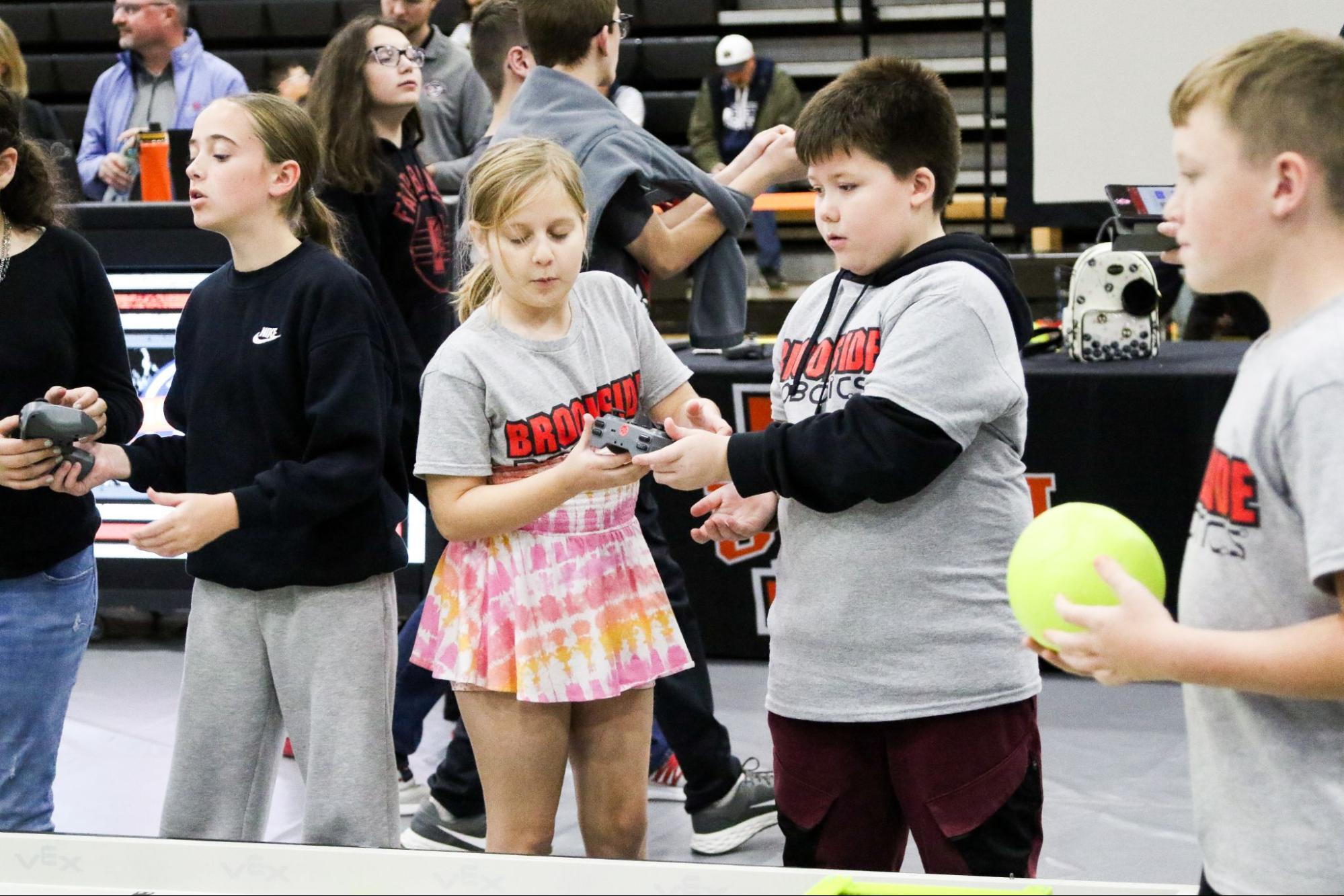 A girl Driver hands off the controller to the boy Driver on her team beside the field during the match.