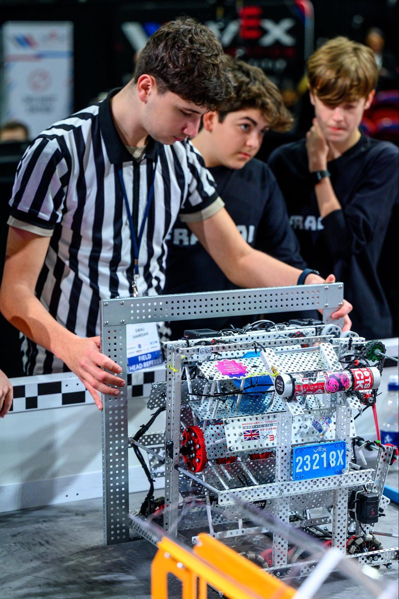 A referee holds a sizing tool up to a v 5 robot before a match.
