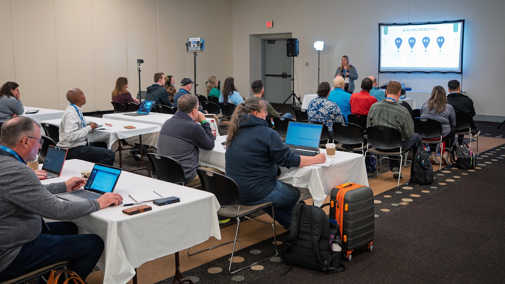 Educators seated at tables during a VEX Robotics Educators Conference presentation.